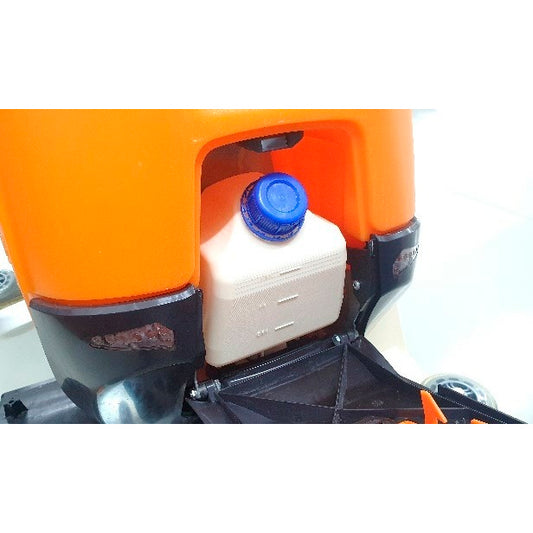 Eine Nahaufnahme des Ultimaxx Intellidose+ Kanisters von Diversey Deutschland GmbH & Co. OHG zeigt den weißen quadratischen Behälter mit blauem Schraubverschluss in einem orangefarbenen Fach, umgeben von schwarzen und metallischen Teilen.