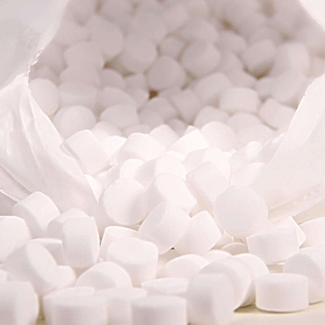 Un primo piano mostra un sacchetto di plastica bianco con la scritta «K+S Minerals and Agriculture GmbH», contenente pastiglie di sale da ebollizione Regenit conformi alla norma EN 973, tipo | sacco (25 kg), che cadono su una superficie. Le pastiglie, piccole e rotonde, hanno forma e dimensioni uniformi e sono ideali per l’impiego negli impianti di addolcimento dell’acqua.