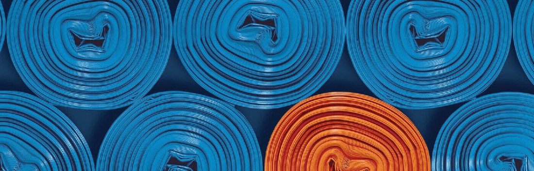 Mehrere aufgerollte blaue Matten von oben, eine orange Matte sticht farblich hervor, gleichmäßig angeordnet im Muster