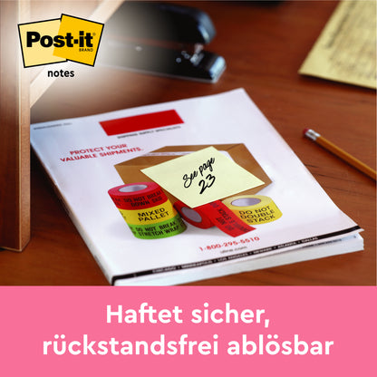 Ein 3M Post-it® Notizblock (gelb, 76x76 mm) mit der Aufschrift "Siehe Seite 23" liegt auf einem Schreibtisch neben Klebebandrollen und einem Stift. Der Text lautet: "Haftet sicher, rückstandsfrei ablösbar." Packung: 16+4 gratis, 100 Blatt/Block, PEFC-zertifiziert.