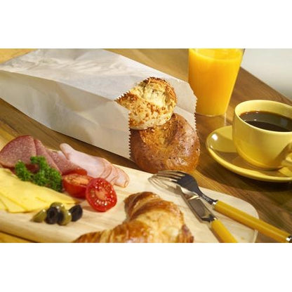 Ein Frühstücksbuffet mit Käsescheiben, Aufschnitt, Tomaten, Oliven, einem Croissant, Brötchen in einem PAPSTAR 1000 Papierfaltenbeutel der PAPSTAR GmbH, schwarzem Kaffee, Orangensaft und Besteck, angeordnet auf einem Holztisch.