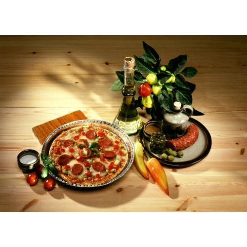 Una pizza ai peperoni viene servita su un piatto accanto a vino, salame, olive e prodotti freschi. Cotta professionalmente nelle Starpak 25 Rundformen, Alu rund di Starpak per una conduzione termica ottimale su un tavolo di legno rustico.