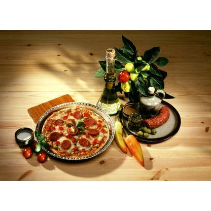 Una pizza ai peperoni viene servita su un piatto accanto a vino, salame, olive e prodotti freschi. Cotta professionalmente nelle Starpak 25 Rundformen, Alu rund di Starpak per una conduzione termica ottimale su un tavolo di legno rustico.