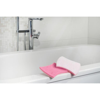 Viene mostrata una vasca da bagno bianca con rubinetti cromati. Sul bordo ci sono una spugna da bagno rosa e una spugna per la pulizia del bagno Scotch-Brite® Bath XXL di 3M Deutschland GmbH. Lo sfondo mostra piastrelle bianche con motivo a mosaico.