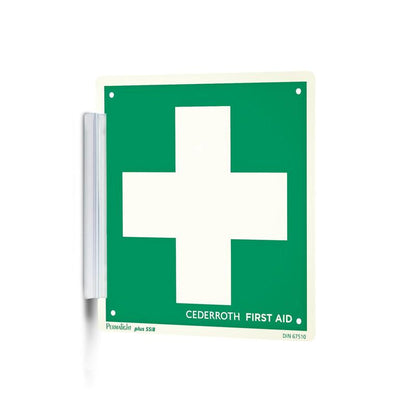 Un "Clip signieren | Packung (1 Stück)" verde e bianco di Orkla Wound Care AB con una grande croce bianca e la scritta "Cederroth First Aid" è fissato al muro come un timbro di firma con un supporto metallico ed è ben visibile sul posto di lavoro.