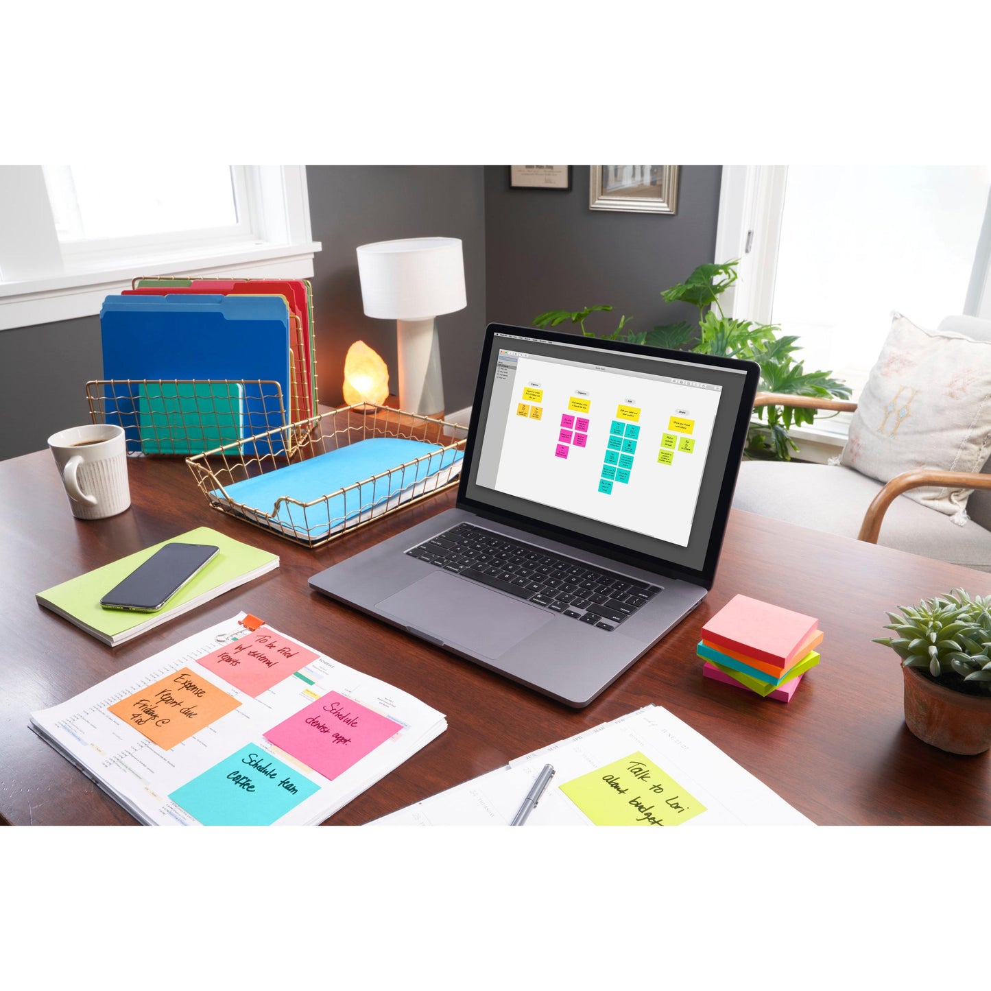 Ein Schreibtisch im Home-Office mit einem Laptop mit digitalen Haftnotizen, farbigen Ordnern, einem Smartphone, einer Lampe, Papieren mit handschriftlichen Notizen, einer Topfpflanze und 3M Deutschland GmbH Post-it® Notes (76x127 mm, 100 Blatt/Block, 6 Blöcke/Packung, 100% PEFC).