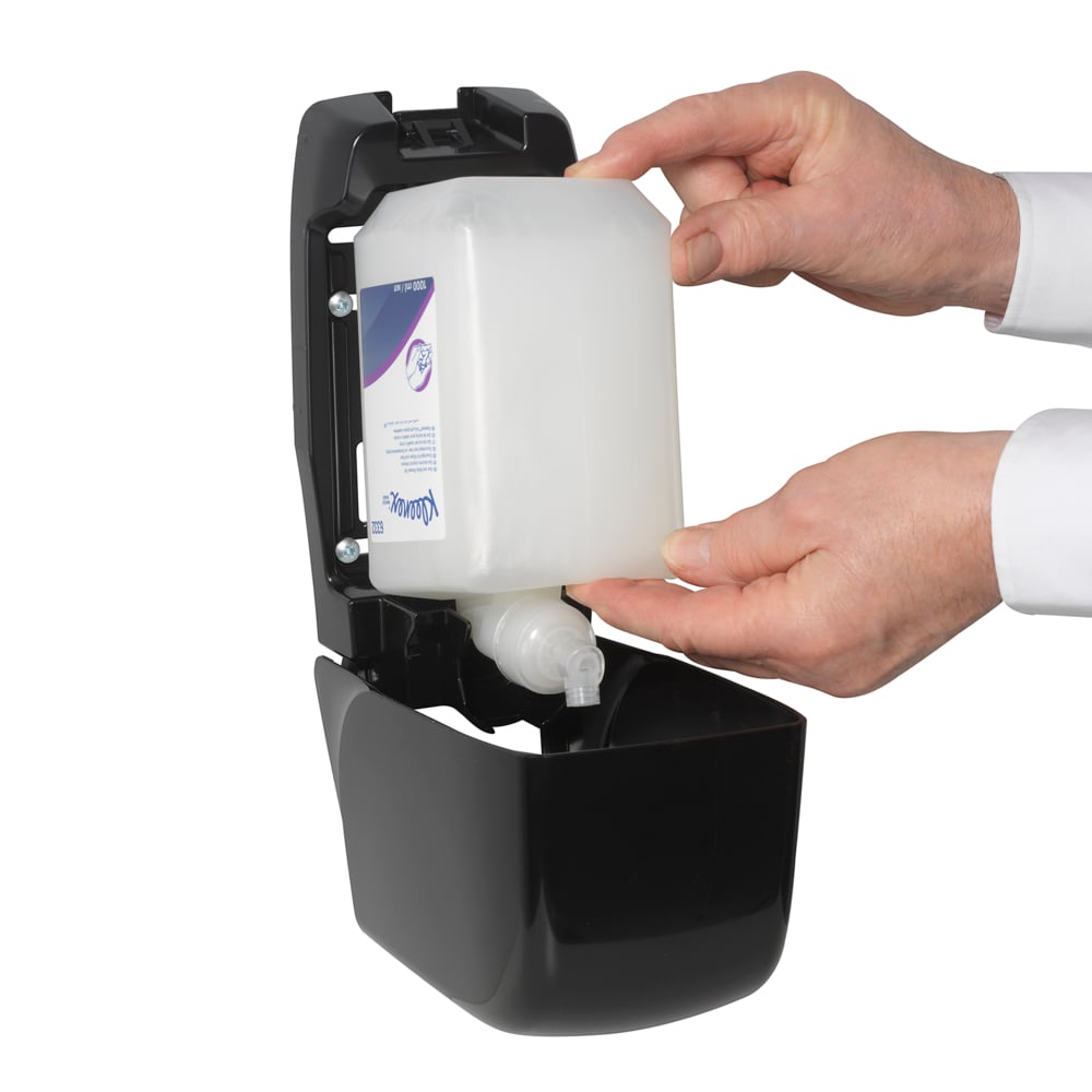 Una persona inserisce una cassetta da 1L di Kleenex® Shampoo per capelli e corpo della Kimberly-Clark GmbH in un distributore a parete nero aperto e utilizza entrambe le mani per garantire una cura delicata e una pulizia efficace.