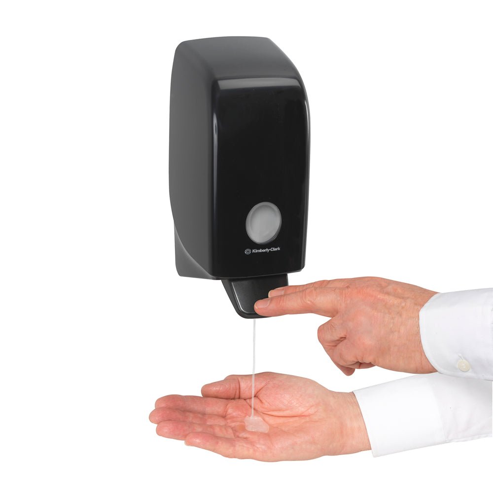 Qualcuno eroga Kleenex® Shampoo per capelli e corpo della Kimberly-Clark GmbH da una cassetta a parete bianca da 1 litro nel palmo della mano e preme la leva per una pulizia efficace e una cura delicata.