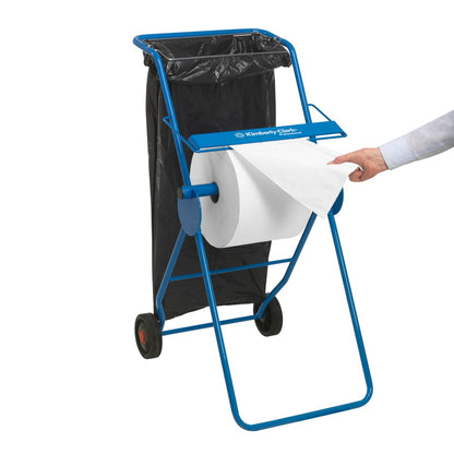 Un dispenser mobile blu con due ruote tiene un rotolo grande di panni WypAll® L10 EXTRA (bianco, 1500 fogli) di Kimberly-Clark GmbH; un sacco nero per i rifiuti viene fissato, mentre una mano tira un foglio dal rotolo grande.