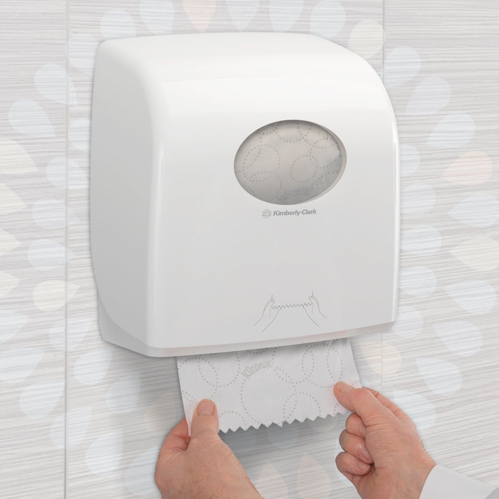 Qualcuno estrae un asciugamano Kleenex® Ultra™ Slimroll™ da un dispenser bianco montato a parete con finestra di visualizzazione e simboli in un bagno piastrellato. Prodotto: scatola da 6 rotoli della Kimberly-Clark GmbH.