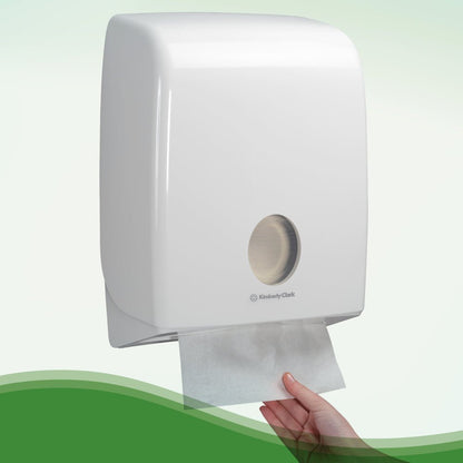 Una mano tira un asciugamano Hostess™ NATURA™ bianco di Kimberly-Clark GmbH da un distributore montato a parete con copertura in plastica bianca e finestra di visualizzazione - ideale per toilette pubbliche. 20 clip x 84 fogli/cartone.