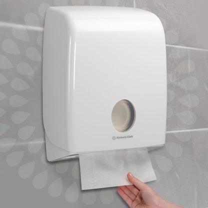 Una mano estrae un fazzoletto piegato Kleenex® - Interfold da un distributore a parete bianco della Kimberly-Clark GmbH in un bagno piastrellato. Il distributore ha una finestra rotonda che offre una vista sui fazzoletti di carta all'interno (15 confezioni x 186 fogli).