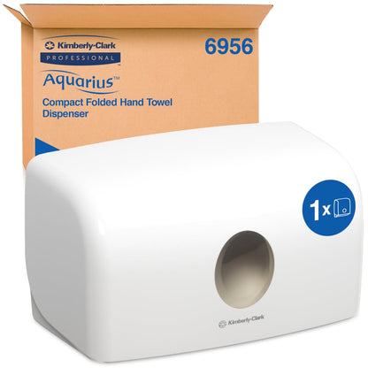 Un distributore bianco Aquarius™ per asciugamani piegati di Kimberly-Clark GmbH (MultiFold, piccolo) si trova davanti al suo imballaggio marrone. Il contenitore compatto garantisce un'estrazione igienica della carta grazie all'apertura rotonda frontale.