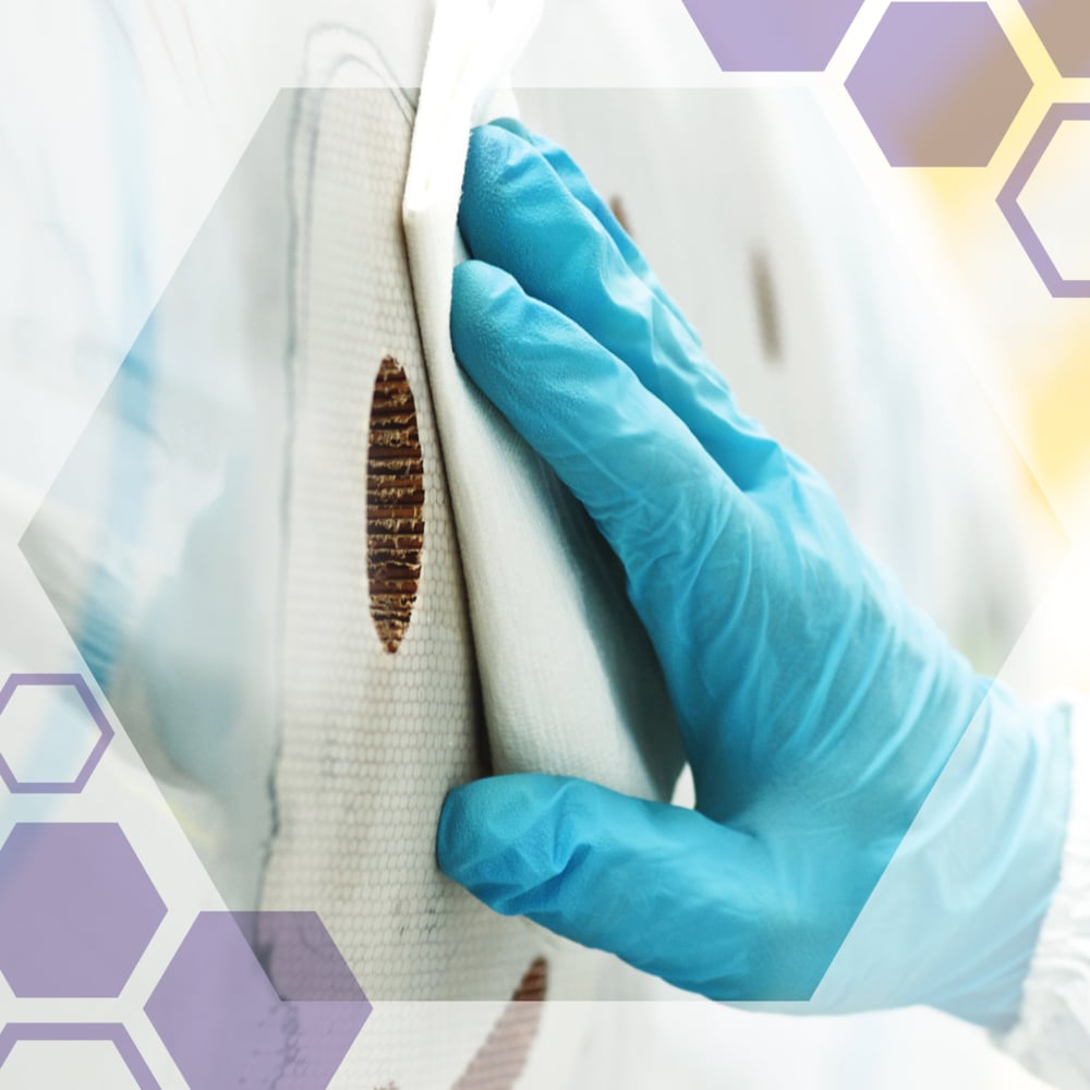 Una mano guantata pulisce una macchia circolare marrone su una superficie bianca con salviette di precisione Kimtech® Science della Kimberly-Clark GmbH. Esagoni semitrasparenti sono sovrapposti all'immagine.