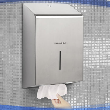 Una mano estrae un asciugamano di carta dal dispenser di asciugamani Kimberly-Clark Professional™ in acciaio inossidabile (1 dispenser), igienicamente montato su una parete piastrellata.