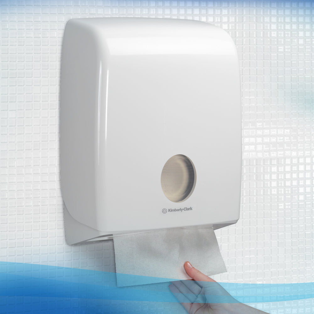 Una mano estrae un asciugamano Scott® - MultiFold / Bianco da un distributore a parete della Kimberly-Clark GmbH in un bagno piastrellato, garantendo così un'asciugatura delle mani igienica.