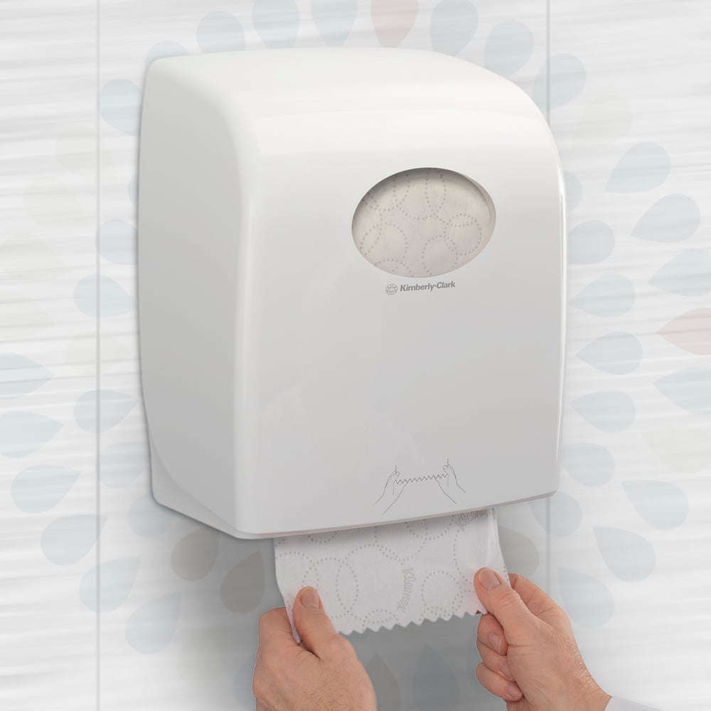 Una persona estrae un rotolo di asciugamani Kleenex® ULTRA™ (Bianco, 150m) di Kimberly-Clark GmbH da un dispenser a parete in un bagno, garantendo così l'asciugatura igienica delle mani. Confezione: 6 rotoli/scatola.