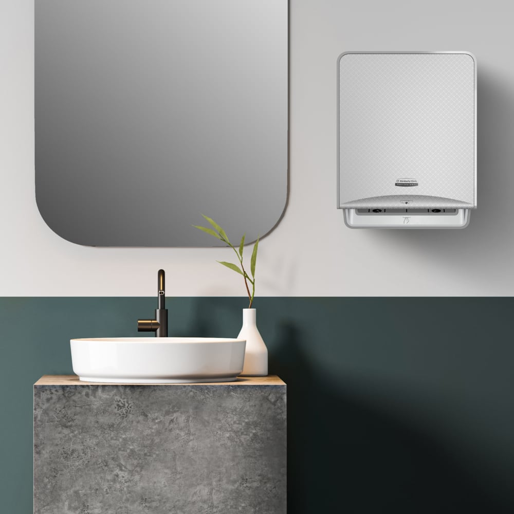 Un bagno moderno con uno specchio quadrato, un lavabo a ciotola su un piano in cemento, un rubinetto nero, un vaso bianco con vegetazione e un dispenser montato a parete per l'asciugatura igienica delle mani con asciugamani Kleenex® della Kimberly-Clark.