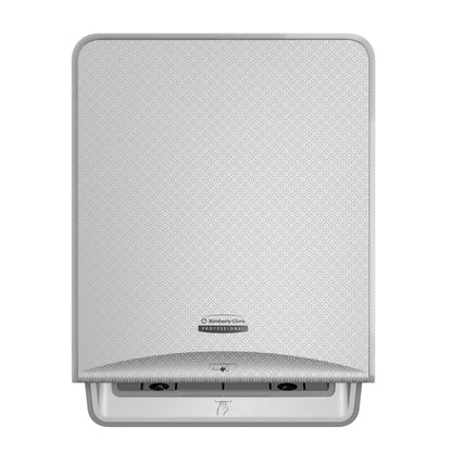 Un mosaico argentato, modulo elettronico No Touch a parete Kimberly-Clark Professional™ Icon™ di Kimberly-Clark GmbH con una placca frontale decorata, logo centrale e una fessura nella parte inferiore per l'erogazione senza contatto degli asciugamani.
