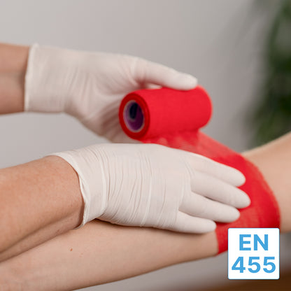 Una persona che indossa guanti in nitrile ARNOMED NITRIL WHITE 200er della ARNOWA GmbH avvolge una benda rossa attorno al braccio di un'altra persona. Nell'angolo in basso a destra è visibile un'etichetta blu-bianca "EN 455".
