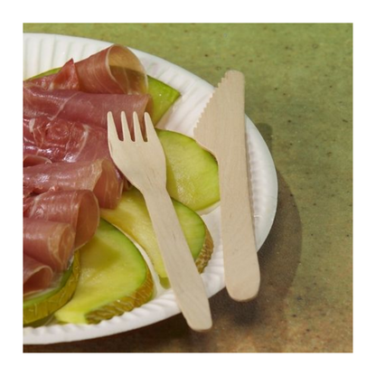 Un piatto di carta bianco con fette di mela verde e prosciutto, accanto a PAPSTAR forchette di legno "pure" 16,5 cm-ecologiche e stabili (100 pezzi)-da PAPSTAR GmbH, insieme a un coltello di legno, su sfondo verde.