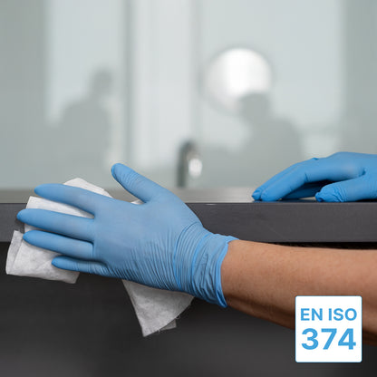 Una persona che indossa guanti monouso ARNOMED NITRIL BLUE XTRA STRONG di ARNOWA GmbH pulisce un piano di lavoro scuro con un panno bianco. È visibile il simbolo EN ISO 374, un ambiente d'ufficio appare sfocato sullo sfondo.