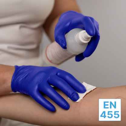 Una persona che indossa guanti monouso in nitrile ARNOMED NITRIL XTRA PURE della ARNOWA GmbH pulisce il braccio di un altro con un panno bianco e una bottiglia spray. L'etichetta "EN 455" appare nell'angolo in basso a destra dell'immagine.