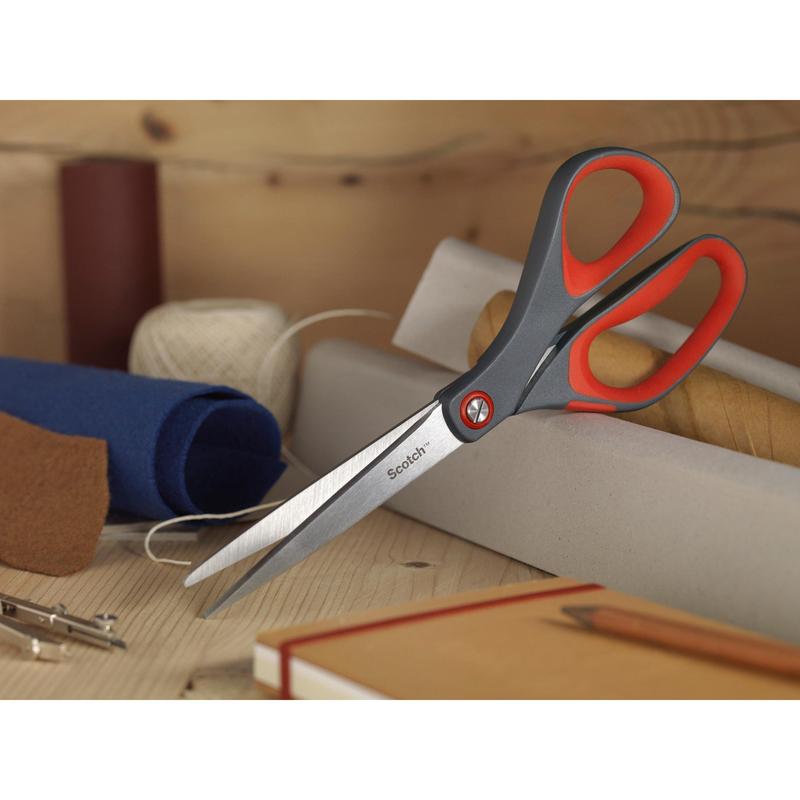 Le forbici di precisione rosse Scotch™ di 3M Deutschland GmbH con manico grigio e rosso si trovano su una superficie di legno tra rotoli di stoffa, una bobina con filo bianco, un quaderno marrone e una matita.