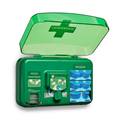 Un distributore di cure per ferite blu di Orkla Wound Care AB è aperto e mostra pacchetti per la pulizia delle ferite, cerotti e un rotolo di bende in schiuma morbida disposti in scomparti separati.