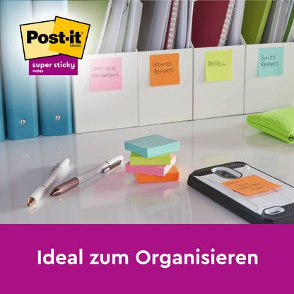 Auf einem Schreibtisch liegen beschriftete Ordner mit farbigen Haftnotizen, Stiften, Ordnern, einem Telefon und einem Stapel 3M Post-it® Super Sticky Z-Notes (76x76 mm, Gelb) in einem PRO Schwarz Spender. Logo oben links; Text unten: "Ideal zum Organisieren.
