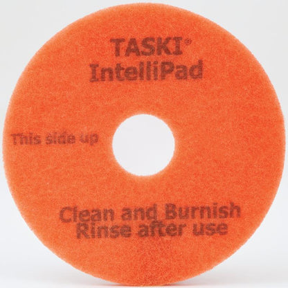 Ein orangefarbenes rundes TASKI Intellipad Kombiniertes Reinigungs- und Polierpad für Unterhaltsreinigung von Diversey Deutschland GmbH & Co. OHG mit einem zentralen Loch. Text: "TASKI IntelliPad. Diese Seite nach oben. Reinigen und polieren. Nach Gebrauch abspülen." Einfacher weißer Hintergrund.