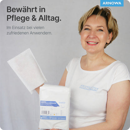 Una donna sorridente in camicia bianca tiene guanti da lavaggio monouso ARNOMED in mollettone di ARNOWA GmbH (confezione, 50 pezzi) con sigillo Dermatest. Testo: "Provato in cura & quotidianità" - ideale per la cura delicata della pelle.