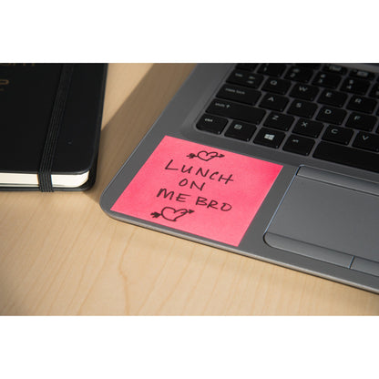 Un cubo di Post-it® Notes (76x76mm, 450 fogli, 100% PEFC) della 3M Deutschland GmbH in rosa è posizionato su una tastiera del laptop con "LUNCH ON ME BRO" e scarabocchi di cuori. Un quaderno nero chiuso è accanto su un tavolo di legno chiaro.