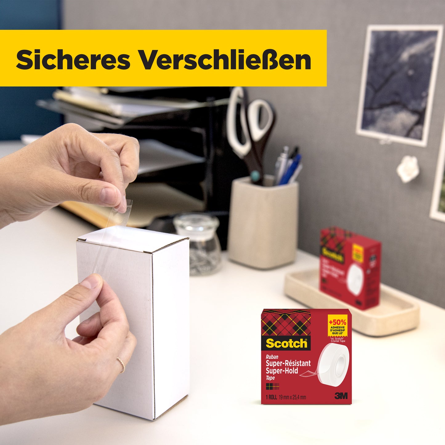 Eine Person verschließt ein weißes Paket am Tisch mit Scotch® Super-Hold Secure Tape, 1 Rolle, 19 mm x 25,4 m von 3M Deutschland GmbH. Im Hintergrund sind Bürobedarf und die Verpackung des transparenten Klebebands zu sehen.