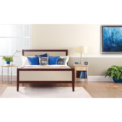 Un letto ben fatto con cuscini bianchi e blu si trova davanti a una parete chiara, coperta con il nastro adesivo per pittori ScotchBlue™ "Multi-Surface" della 3M Deutschland GmbH. Su un comodino ci sono una lampada, un orologio, libri e una pianta in vaso accanto alla finestra luminosa.