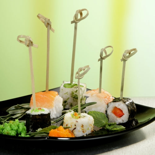 Un piatto nero con vari sushi, ciascun pezzo infilzato con un PAPSTAR 40 spiedino finger food "pure" della PAPSTAR GmbH, guarnito con erbe e uova, su uno sfondo verde-giallo - ideale per mettere in scena accessori da catering.