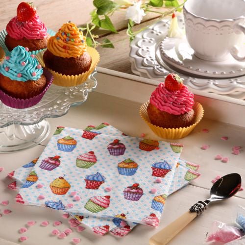 Una tavola apparecchiata con cupcake su un supporto di vetro, un piatto, un cucchiaio, una tazza da tè bianca con piattino, zuccherini rosa a forma di cuore e colorati tovaglioli PAPSTAR 20 tovaglioli 33x33cm 3-strati 1/4 piegato design set 5 di PAPSTAR GmbH.