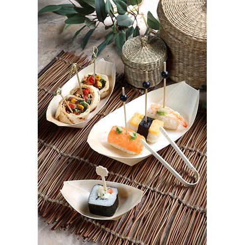 Fingerfood come sushi e wrap su spiedini viene servito nelle 50 ciotole da fingerfood in legno "pure" barchette della PAPSTAR GmbH su un tappetino di bambù con cesti e foglie verdi sullo sfondo.