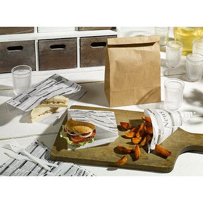 Un tavolo con un sandwich, un hamburger e patate a spicchi, avvolti in PAPSTAR 5 fogli di carta da imballaggio 3 cm x 2 cm "Newsprint" della PAPSTAR GmbH, accanto a un sacchetto di carta marrone, bicchieri e posate di plastica e un tagliere di legno su una superficie bianca.