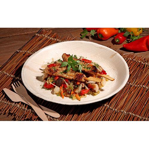 Spiedini di pollo alla griglia con padellata di verdure colorate vengono serviti su un PAPSTAR 6 piatti, foglia di palma „pure“ rotondi di PAPSTAR GmbH - stoviglie ecologiche, presentate con stile su una base intrecciata con posate in legno e peperoni freschi in vista.