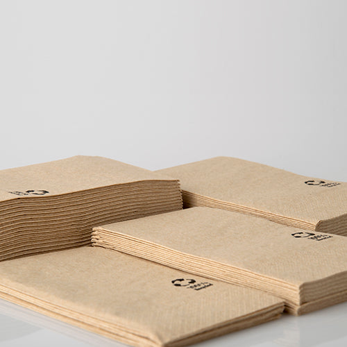 Quattro pile di tovaglioli PAPSTAR a 3 veli, 33x33 cm, naturali, realizzati in carta riciclata (100 pezzi) di PAPSTAR GmbH si trovano su una superficie bianca. Ogni tovagliolo riciclato è dotato di un piccolo simbolo di riciclaggio nero nell'angolo.