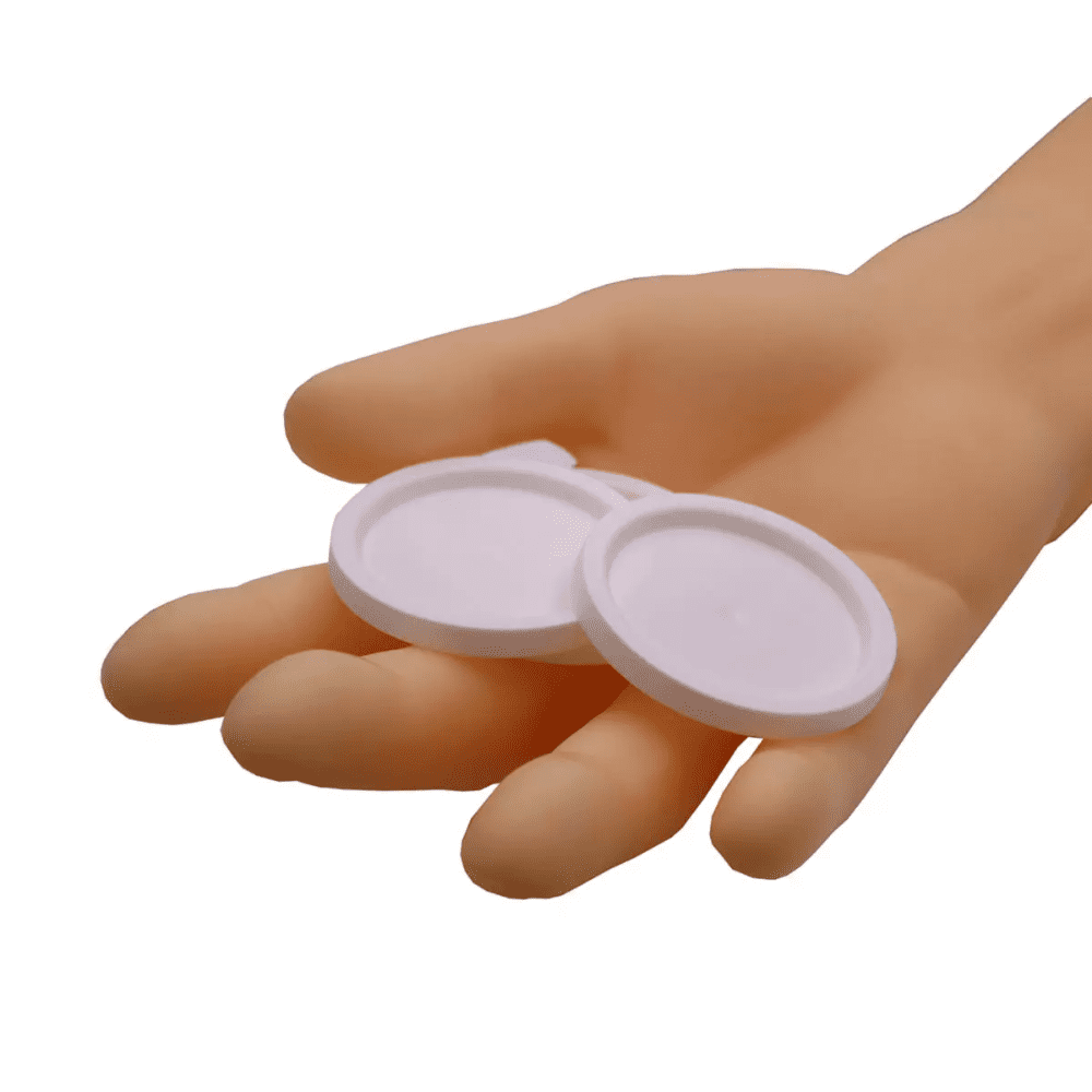 Una mano tiene due coperchi rotondi AMPri per bicchieri da medicina, oggetti bianchi su uno sfondo bianco semplice.