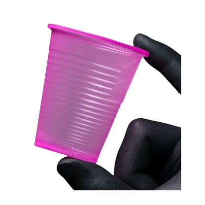 Un piccolo bicchiere da risciacquo AMPri Dental PP rosa in polipropilene è tenuto tra due dita guantate davanti a uno sfondo bianco. Questo bicchiere monouso della AMPri Handelsgesellschaft mbH, spesso trovato negli studi dentistici, presenta una superficie strutturata con scanalature orizzontali.