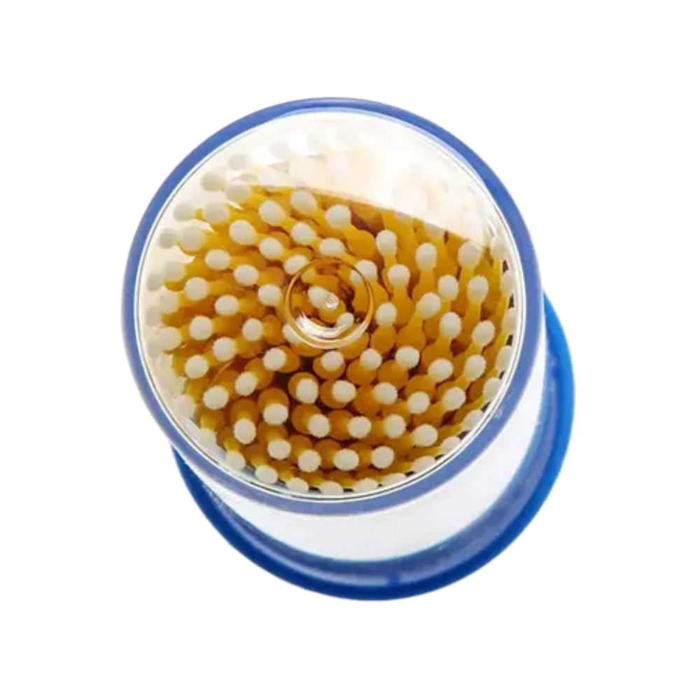 Una vista dall'alto mostra gli applicatori monouso AMPri MED-COMFORT, ideali per lavori precisi. Questi applicatori sono ordinatamente disposti in un motivo circolare, con punte bianche e steli marroni. Il contenitore trasparente ha una base o coperchio blu che ricorda i prodotti di base per esigenze dentali.