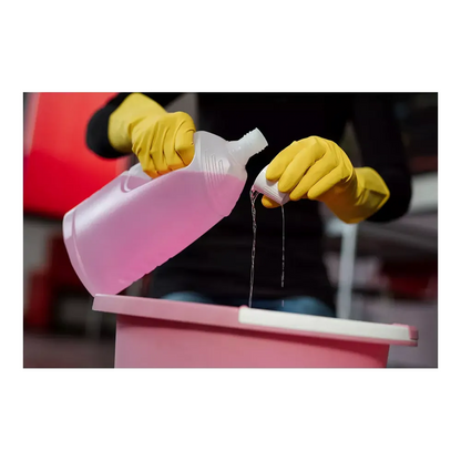 Una persona che indossa guanti di protezione chimica AMPri SolidSafety ChemL della AMPri Handelsgesellschaft mbH versa del liquido da una bottiglia di plastica trasparente in un piccolo coperchio sopra un contenitore rosa. Il liquido, forse una soluzione detergente AMPri, si distingue dallo sfondo sfocato.