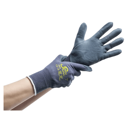 Una persona indossa un guanto blu scuro rivestito in gomma sulla mano destra e infila un guanto abbinato sulla sinistra. Questi guanti da montaggio ultraleggeri AMPri SolidSafety Tough Micro Touch, disponibili nelle taglie dalla S alla XXL e prodotti dalla AMPri Handelsgesellschaft mbH, sono stampati con testo e simboli gialli sul dorso. Lo sfondo è semplicemente bianco.