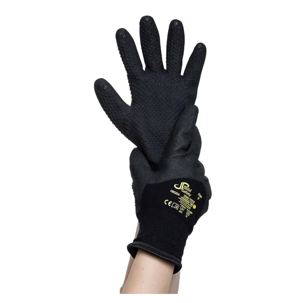 Una coppia di guanti protettivi neri AMPri SolidSafety Tough Winter Dots, resistenti al freddo e dotati di palmi testurizzati, viene tenuta sollevata da una mano. Questi guanti, pensati per migliorare la motricità fine, recano sul dorso il marchio giallo e i simboli di certificazione di sicurezza della AMPri Handelsgesellschaft mbH.