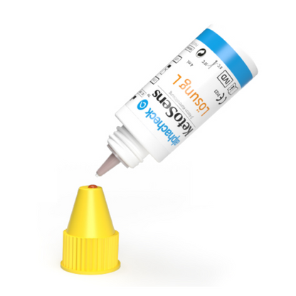 Un flacone bianco con etichetta blu-gialla è capovolto, con l'ugello sopra un tappo giallo. L'etichetta contiene testo e simboli che indicano probabilmente che si tratta di un prodotto Alphacheck KetoSens β-Keton-Soluzione di controllo L+M | Confezione (2 flaconcini) di Berger Med GmbH per l'uso con dispositivi di misurazione chetogenica.