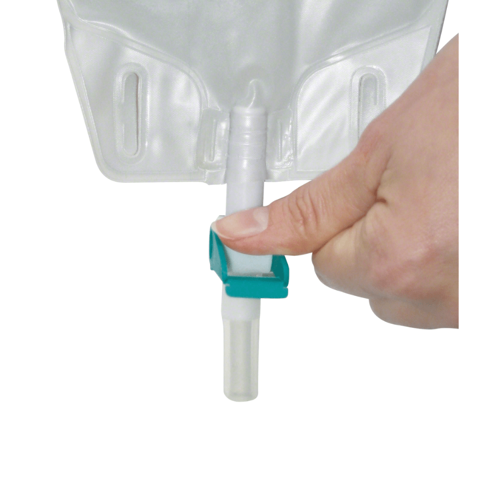 Una mano afferra una valvola vicino all'apertura di un sacchetto per gamba Urimed® B'Bags, 500 ml, un sacchetto di plastica trasparente per il trattamento dell'incontinenza urinaria. La valvola con una clip verde regola il flusso di liquidi dal sacchetto senza DEHP di B. Braun Deutschland GmbH & Co. KG.
