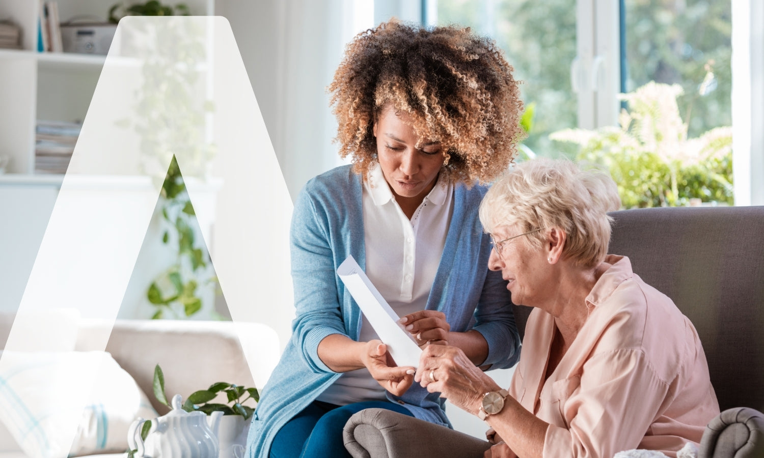 Eine jüngere Frau zeigt einer älteren Frau, die auf einer Couch in einem hellen Wohnzimmer sitzt, ein Dokument oder ein Tablet. Sie scheinen gemeinsam Informationen zu besprechen.